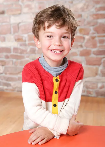 Junge im rot-weißen Pullover vor einer Backsteinwand